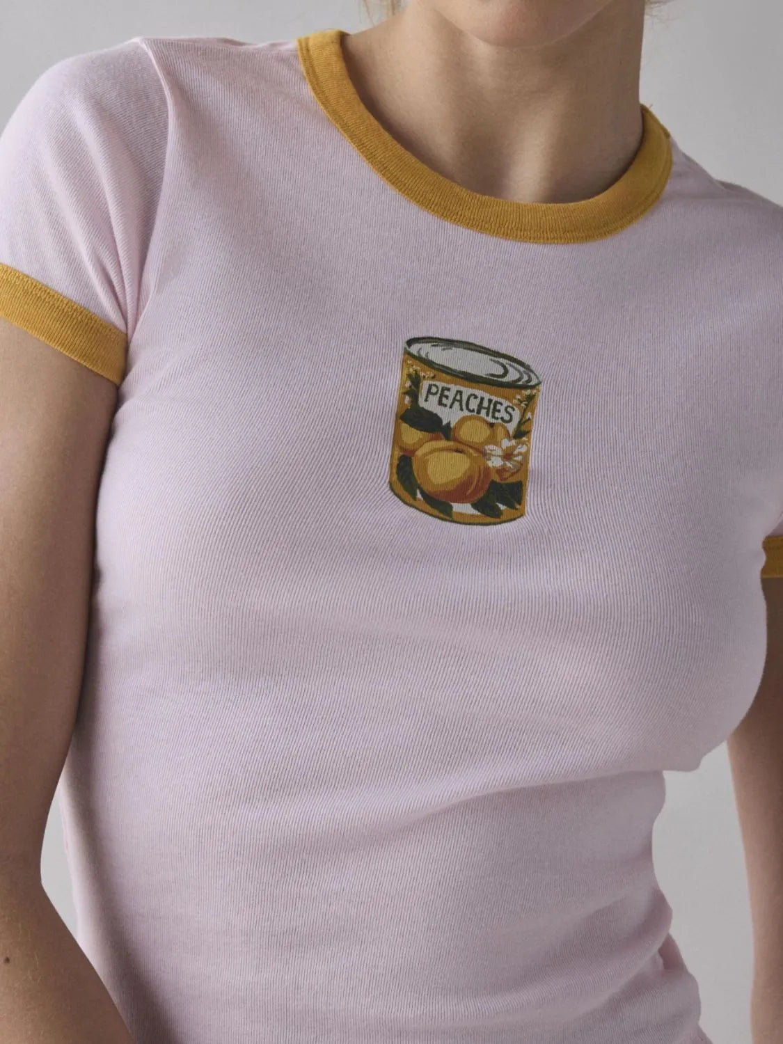 Soft baby pink ringer tee with yellow accents and canned peaches graphic on the front.