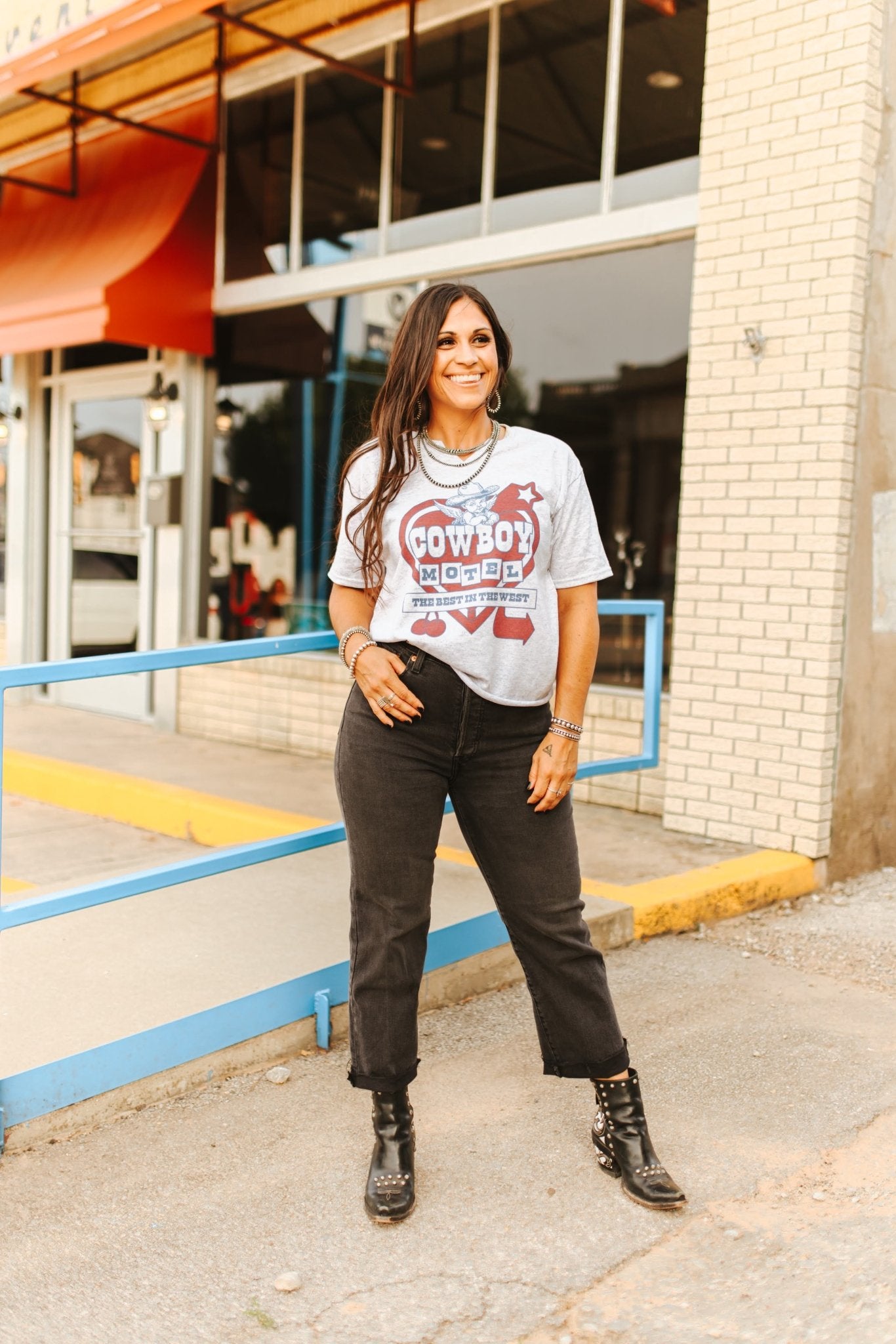 Woman wearing a graphic t-shirt and jeans standing on a sidewalk.