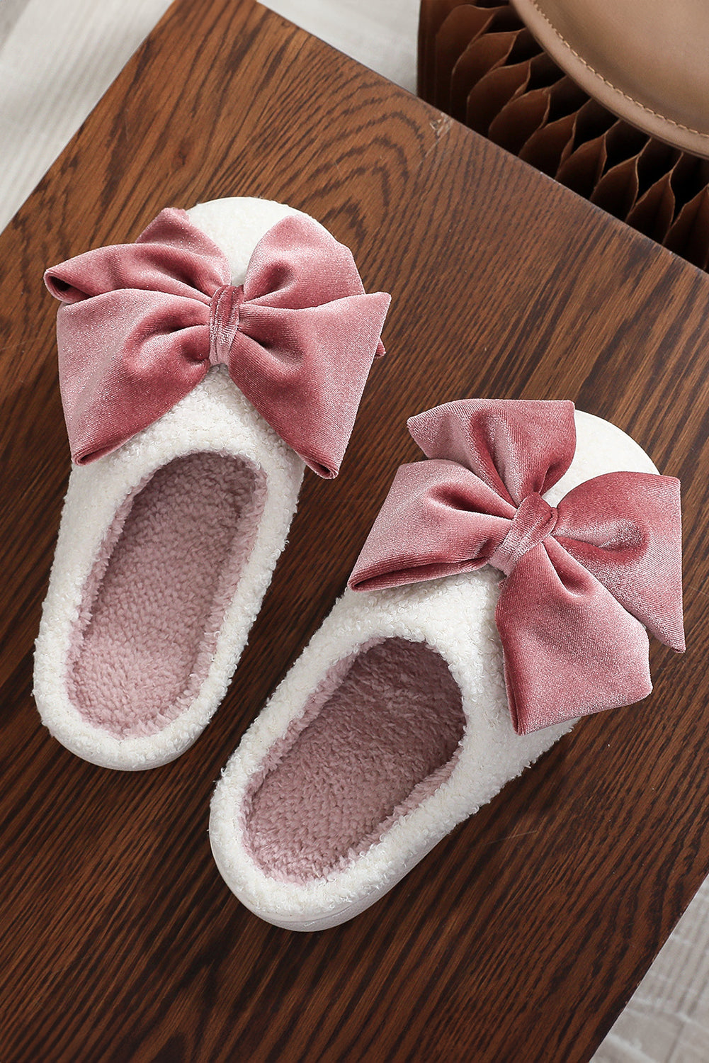 White slippers with pink velvet bows on a wooden surface