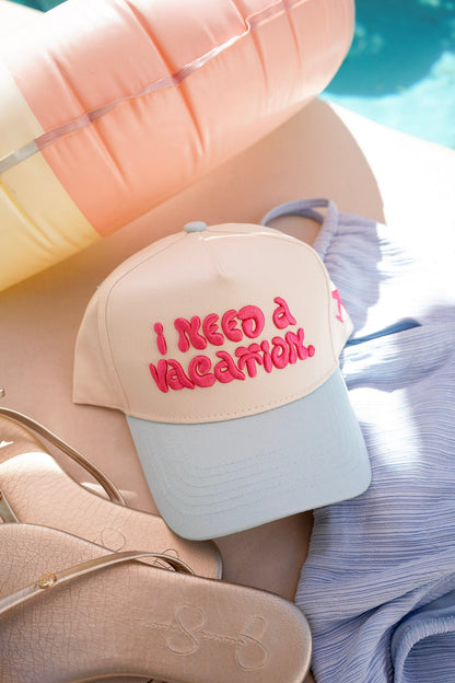 Beige and light blue cap with 'I Need a Vacation' text on a beach setting.