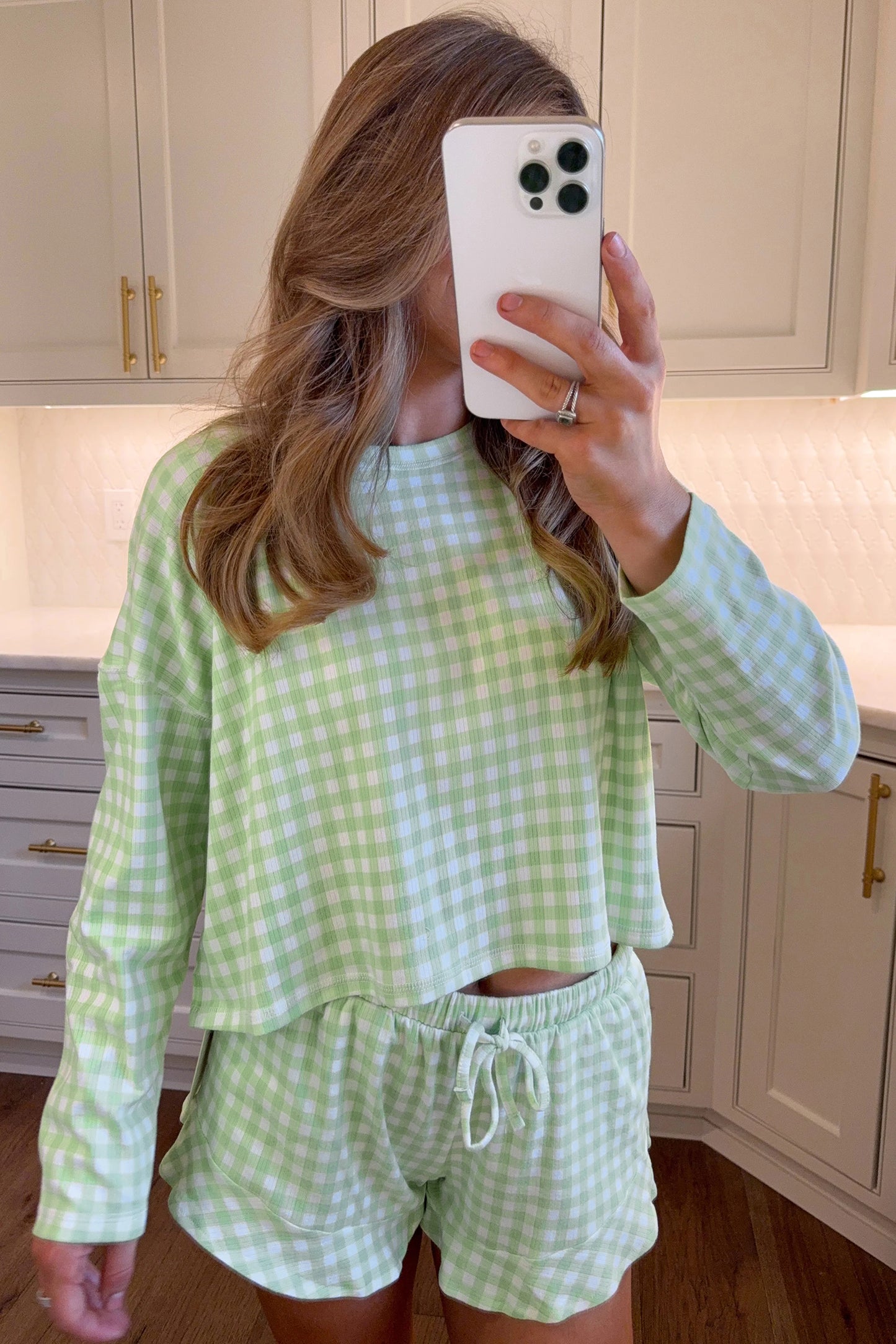 Person wearing a green and white checkered outfit taking a mirror selfie in a kitchen.