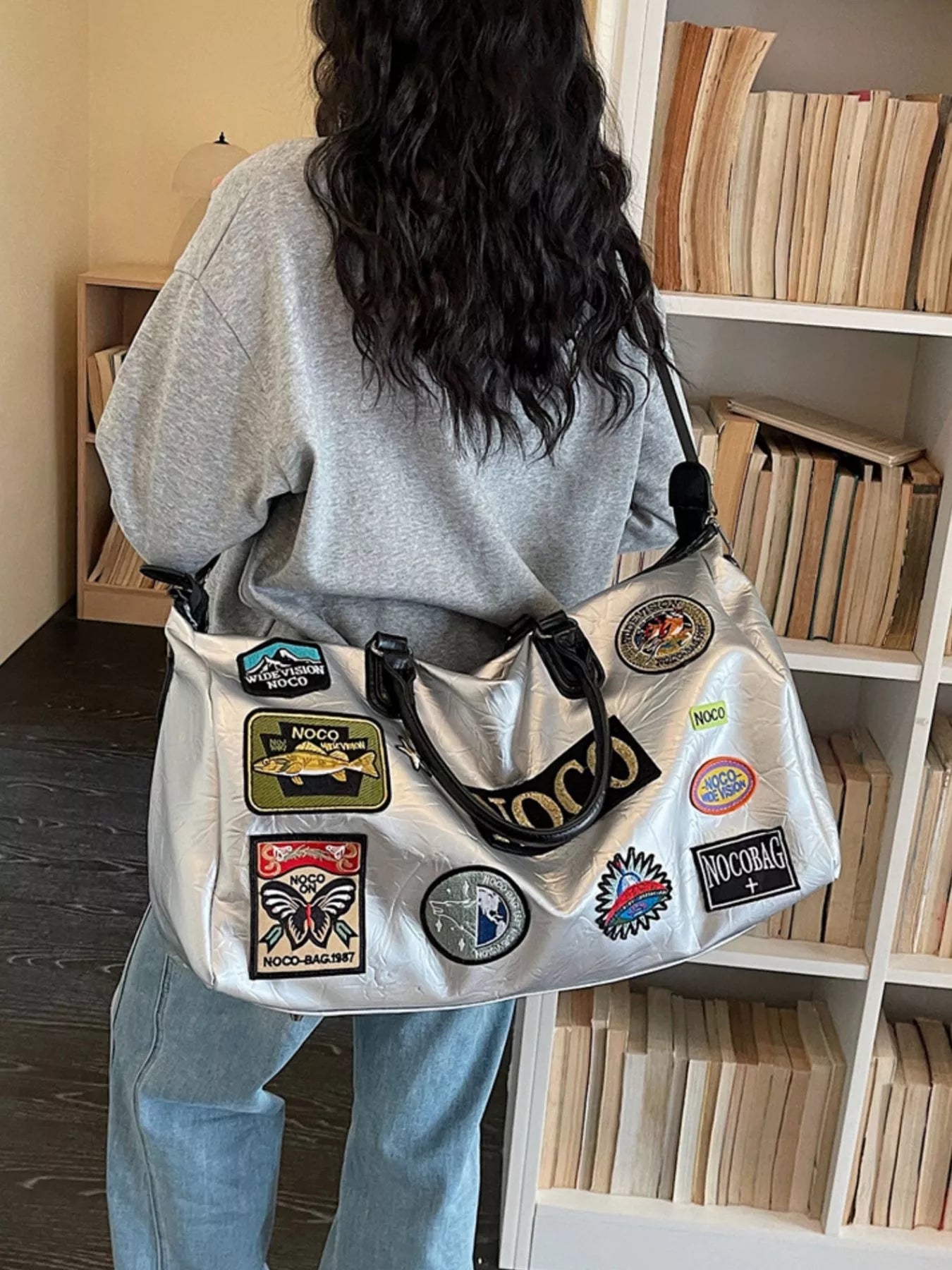 Person wearing a gray bag with patches in a room with bookshelves.