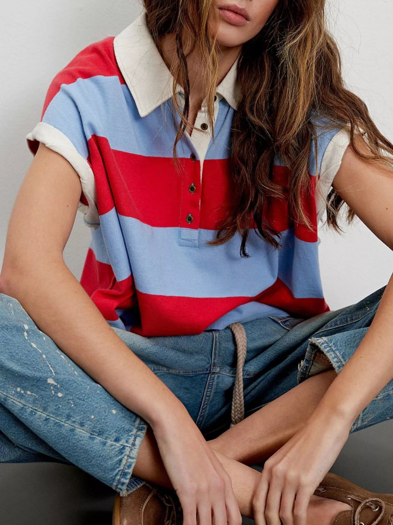 Person wearing a colorful striped polo shirt and jeans sitting on a chair.