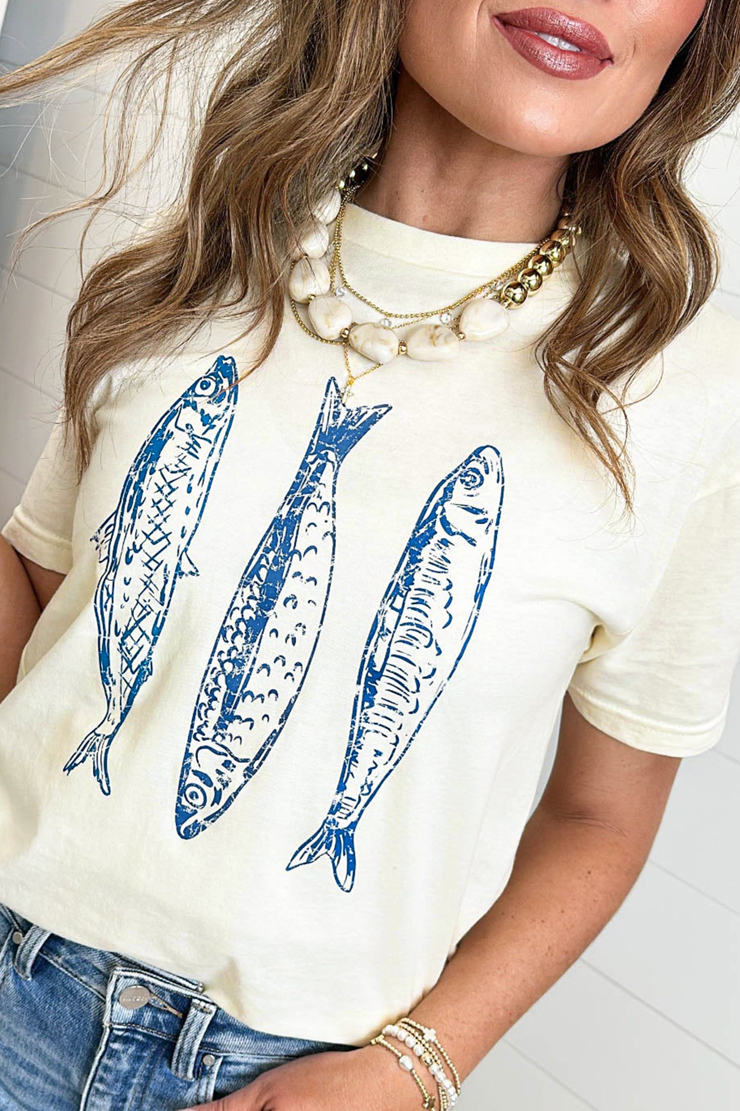 Woman wearing a white t-shirt with blue fish illustrations and gold jewelry.