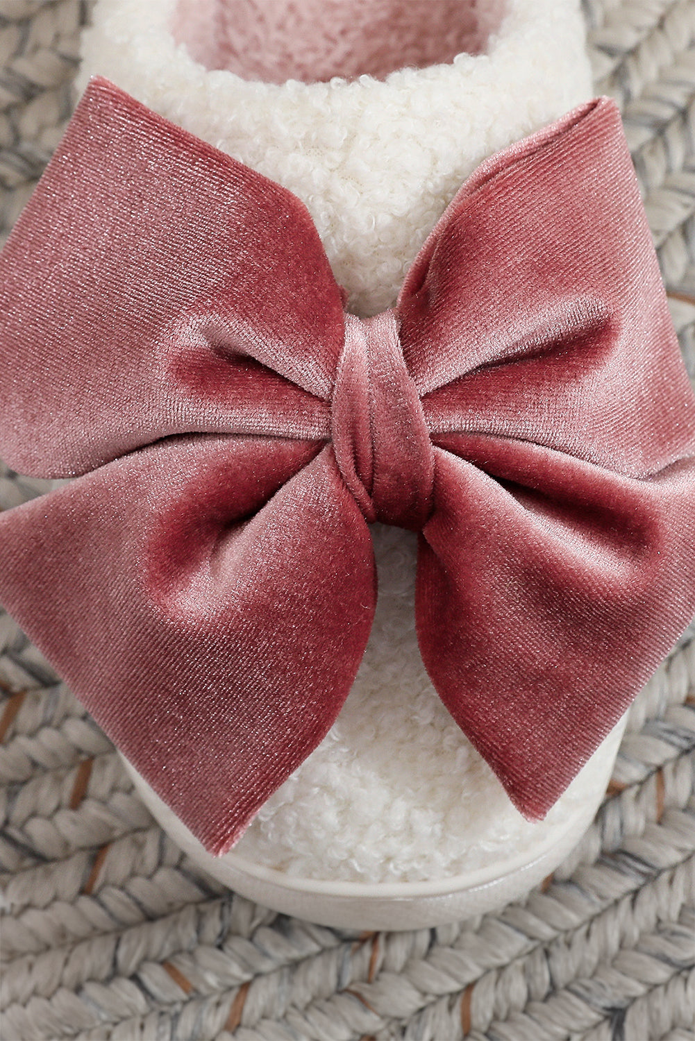 White slipper with a large pink bow on a textured surface