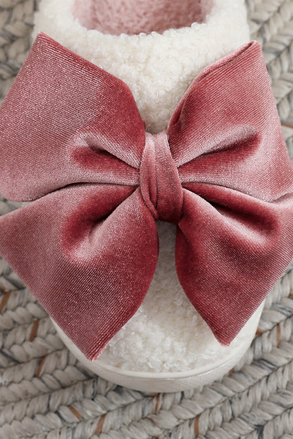 White slipper with a large pink bow on a textured surface