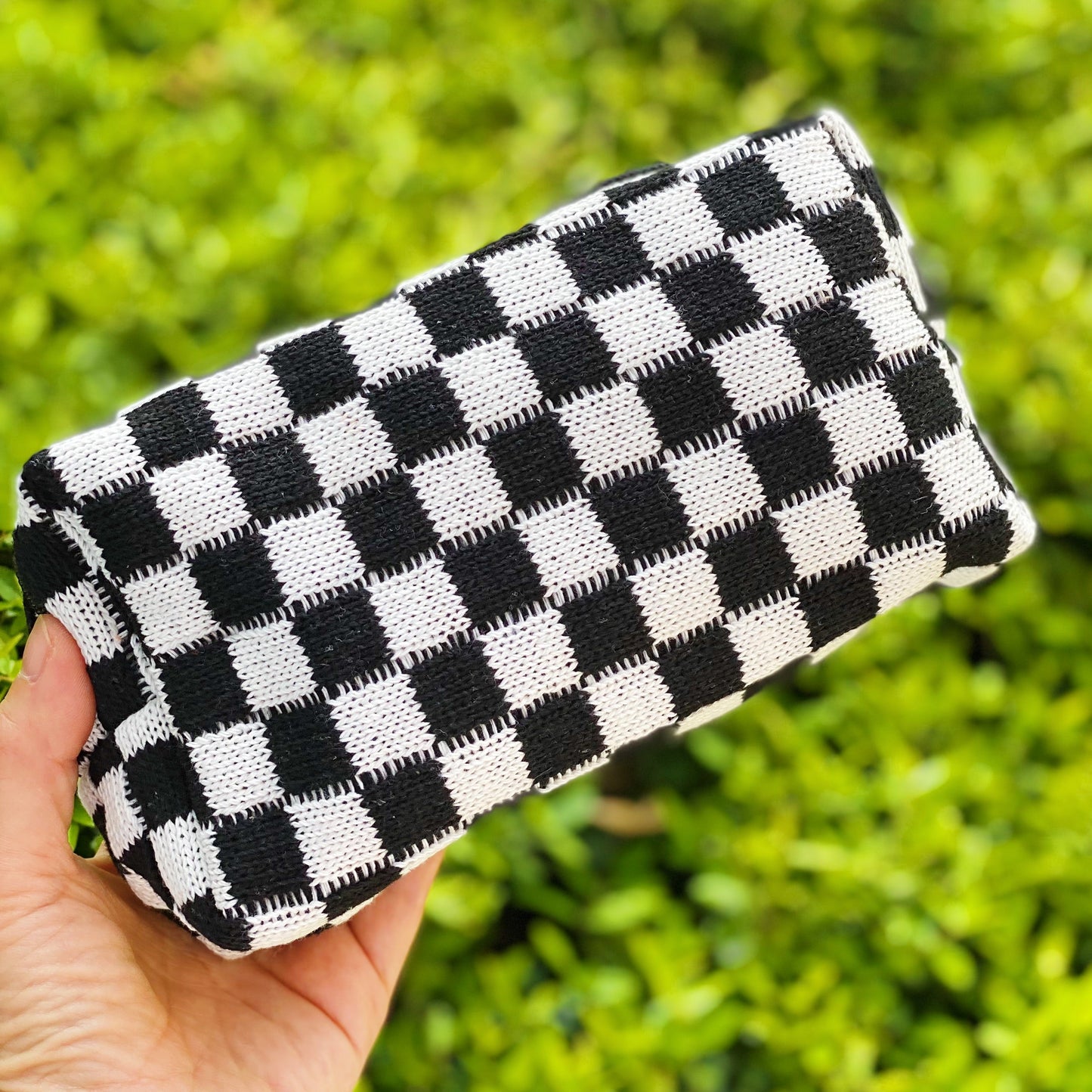 Black and white checkered clutch held by a hand with a green blurred background
