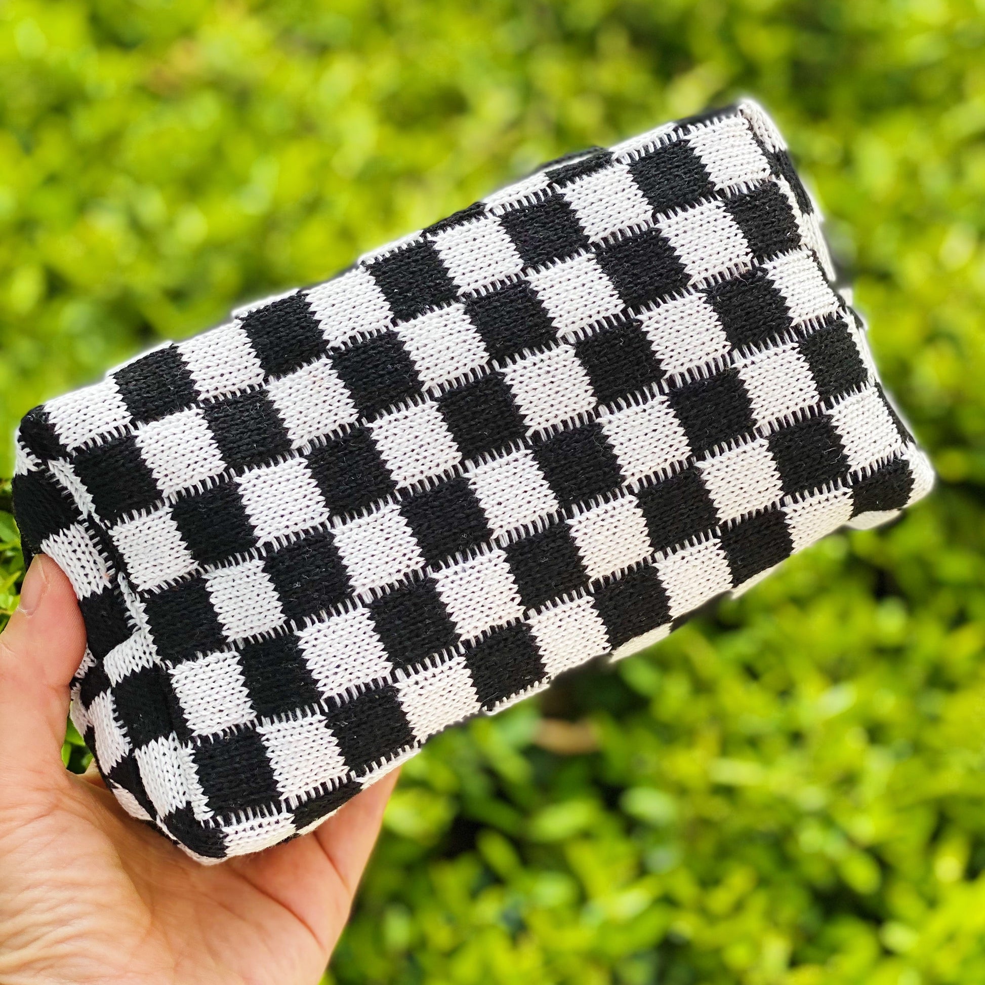 Black and white checkered clutch held by a hand with a green blurred background