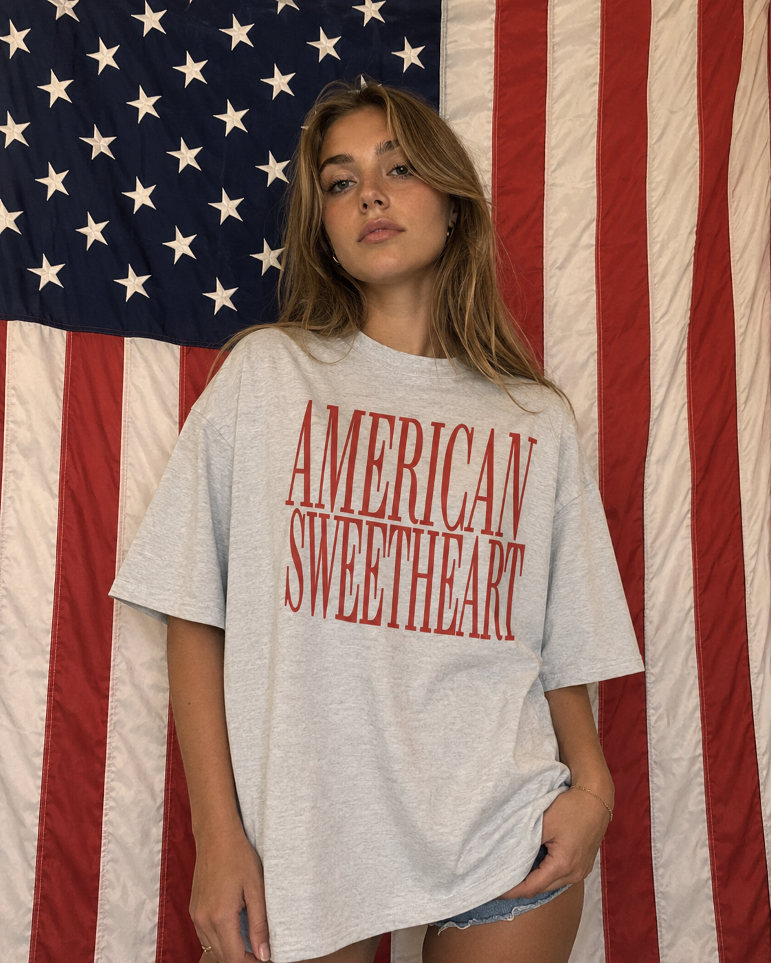 Woman wearing a 'American Sweetheart' t-shirt in front of an American flag