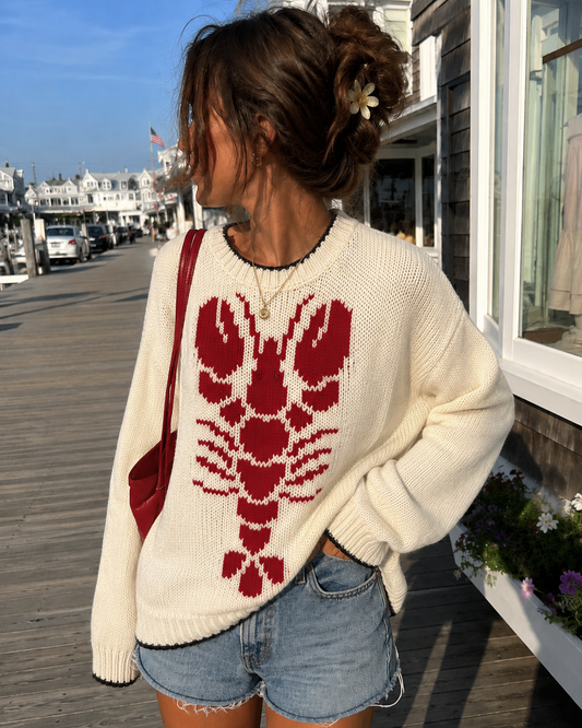 Person wearing a white sweater with a red lobster design on a boardwalk.