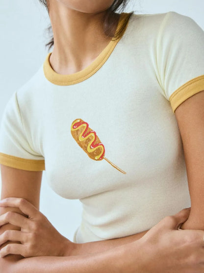 White and yellow ringer baby tee featuring a printed corndog graphic on the chest.