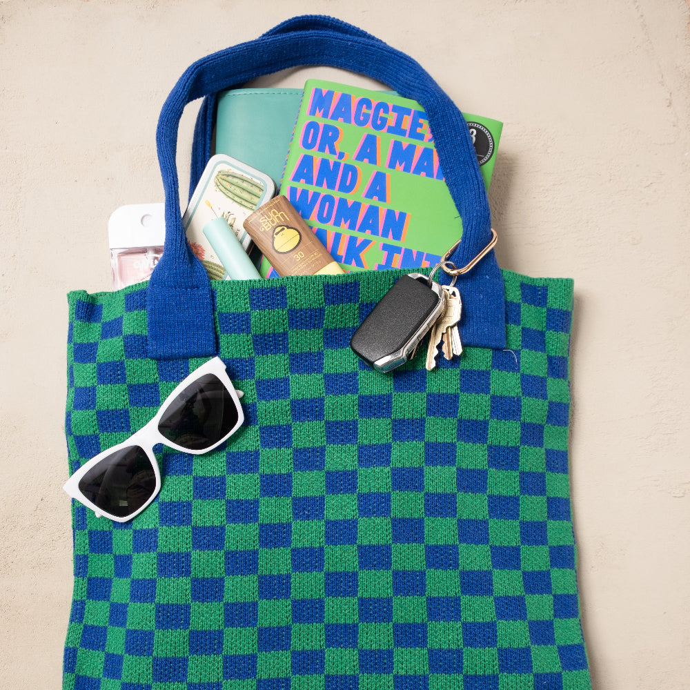 Green and blue checkered tote bag with sunglasses, wallet, and keys on a beige background
