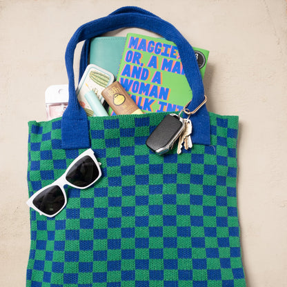 Green and blue checkered tote bag with sunglasses, wallet, and keys on a beige background