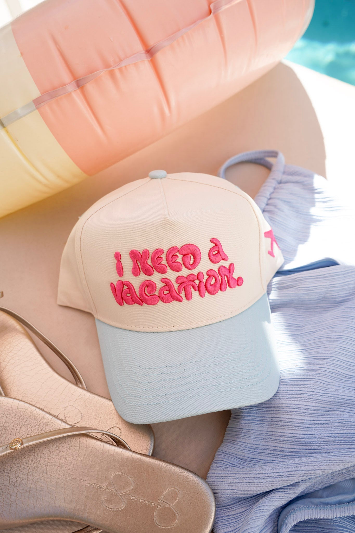 Beige cap with 'I Need a Vacation' text on a beach setting