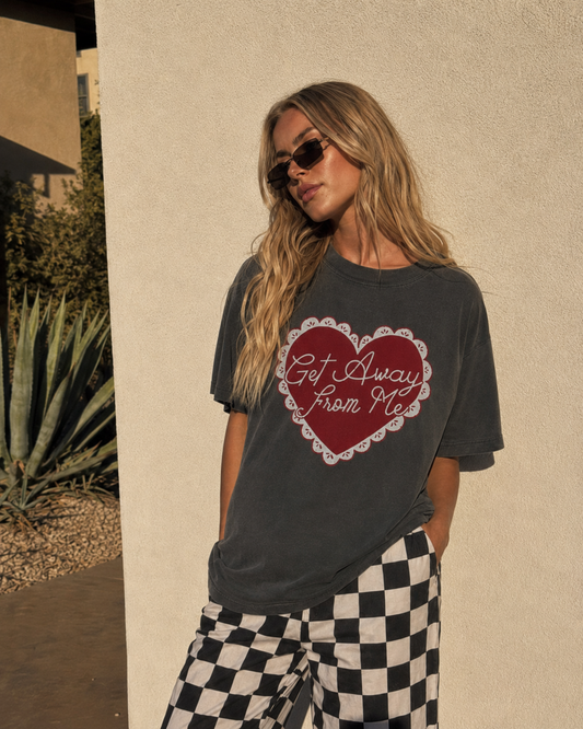 Girl wearing Get Away From Me Graphic Tee with black and white checkered pants in the desert
