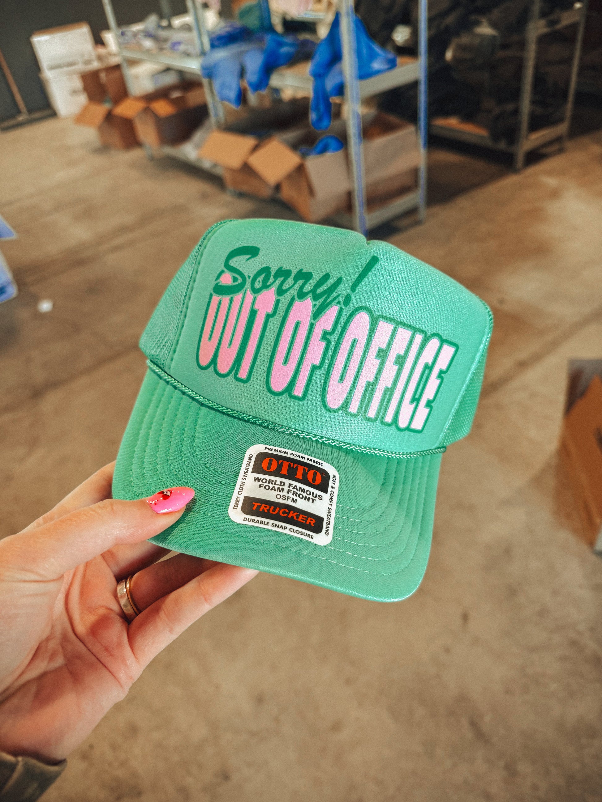 Green cap with 'Sorry! Out of Office' text held by a hand in an indoor setting.