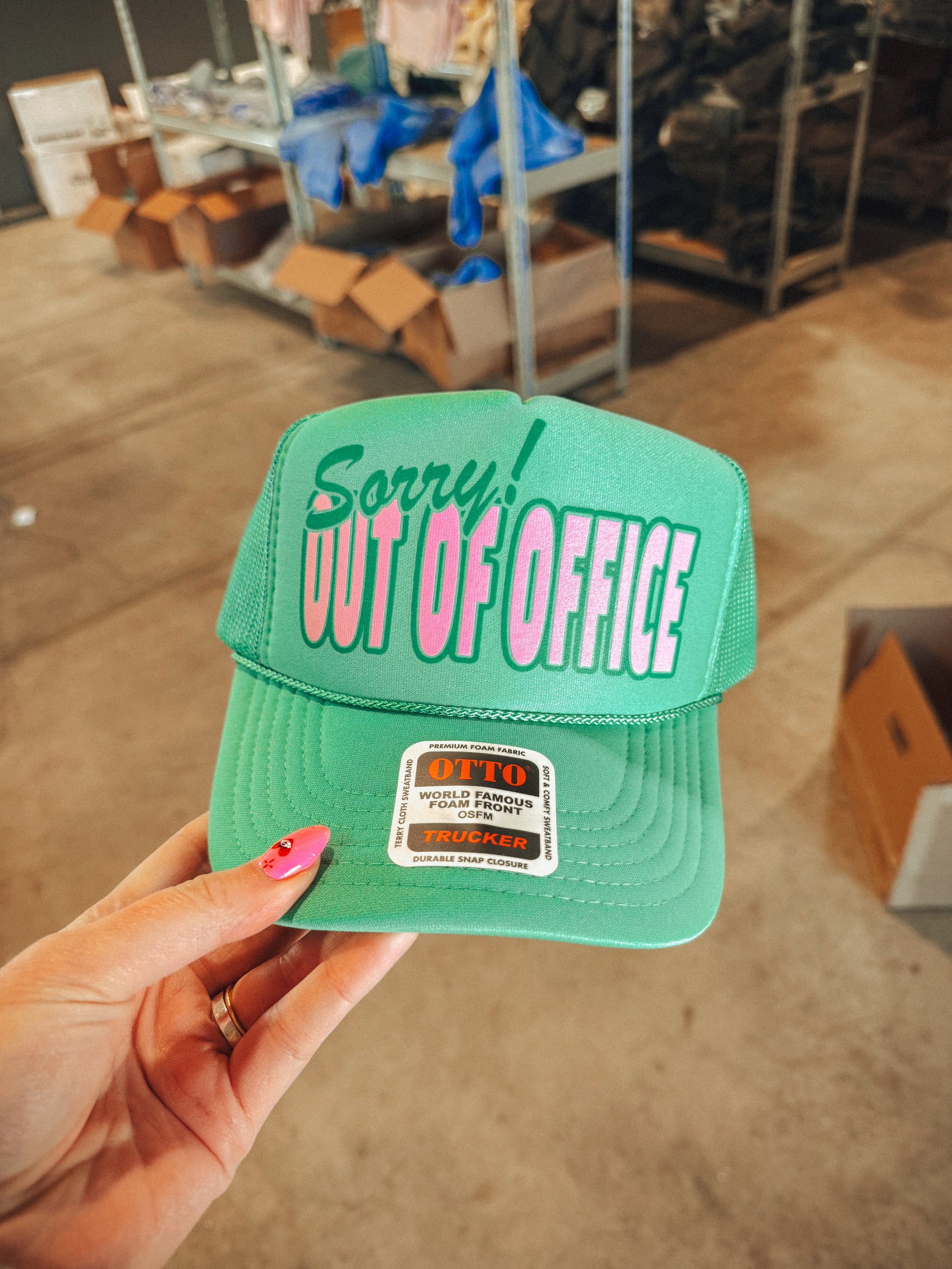 Green cap with 'Sorry! Out of Office' text held by a hand in an indoor setting.