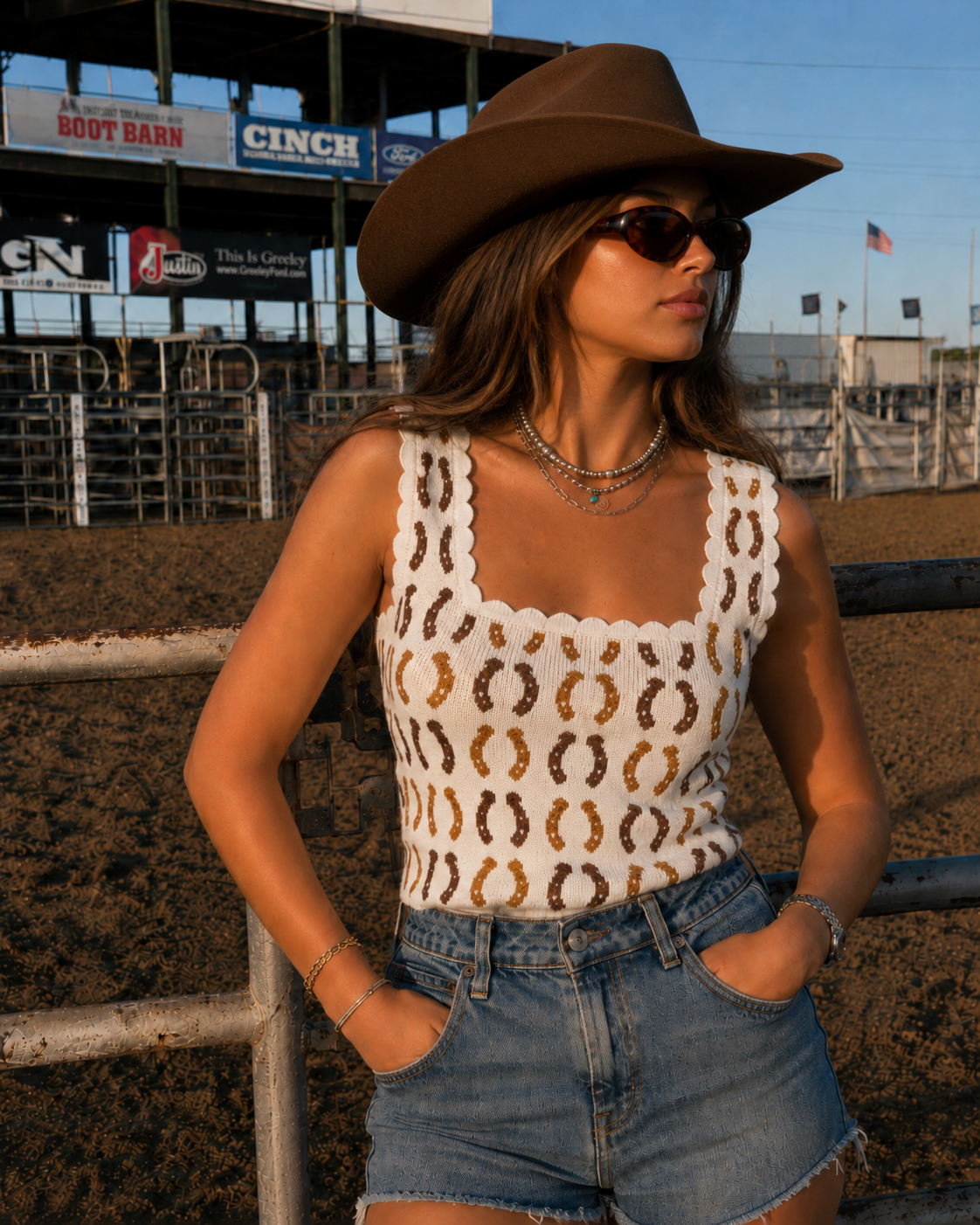 Woman in a cowboy hat and patterned top standing in a rodeo arena.