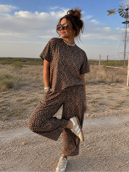 Woman in leopard print outfit standing in a desert landscape with a windmill in the background