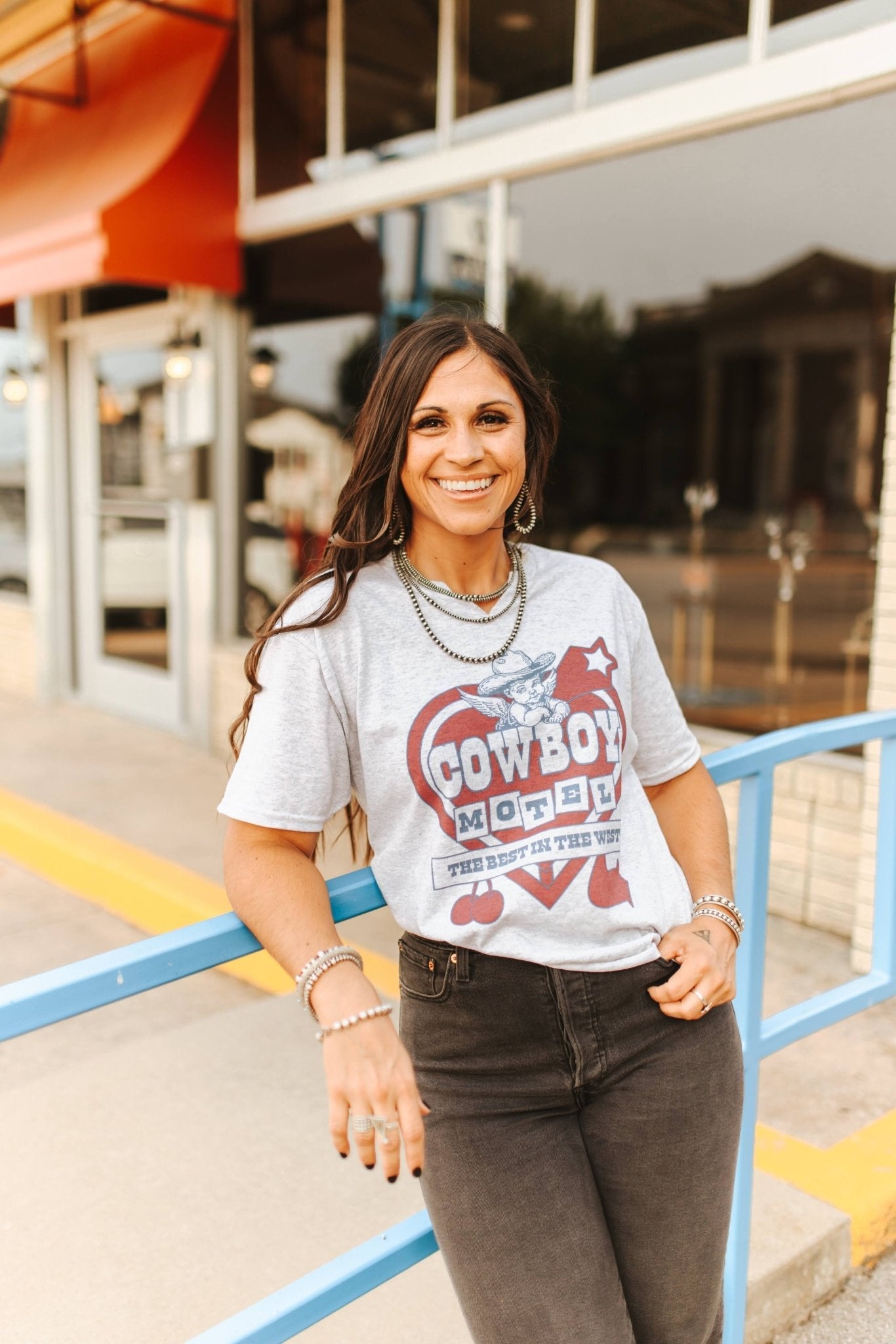 Woman wearing a graphic t-shirt with text and graphics, standing outdoors.