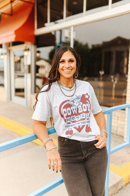 Woman wearing a graphic t-shirt with text and graphics, standing outdoors.