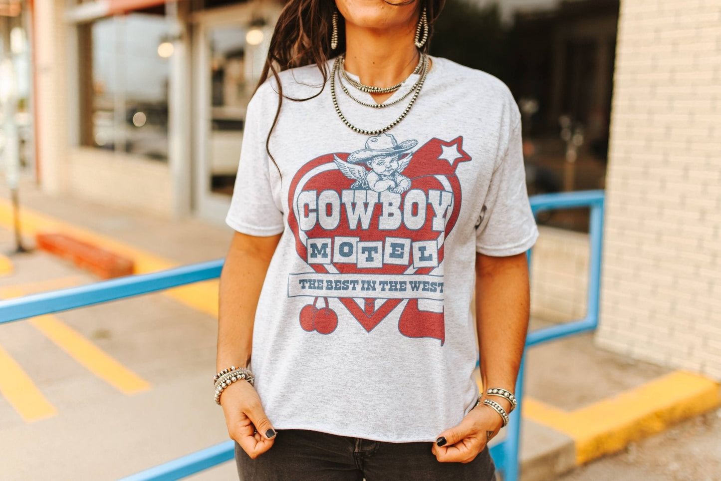 Person wearing a t-shirt with 'Cowboy Motel' design outdoors.