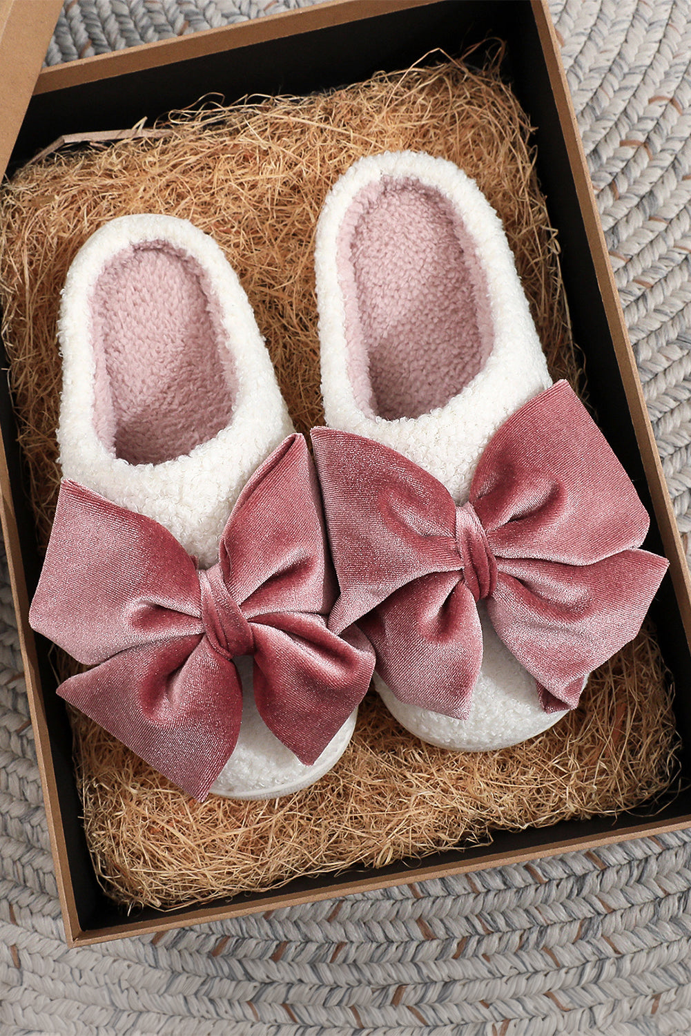 White slippers with pink velvet bows in a box on a textured surface