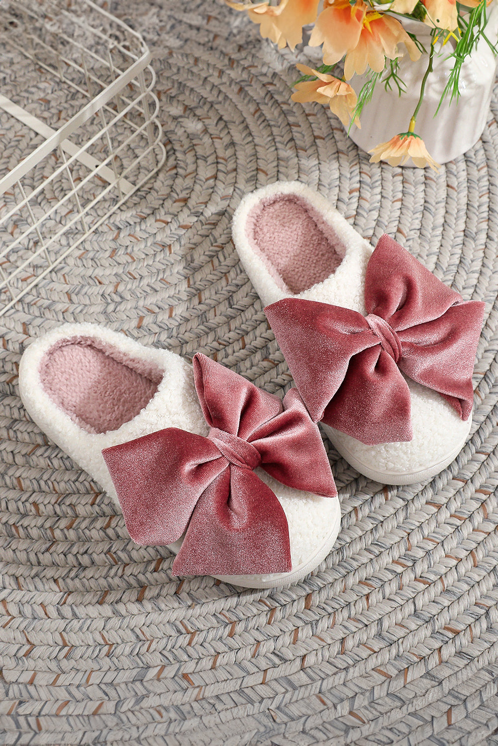 White slippers with pink bows on a textured surface with flowers in the background