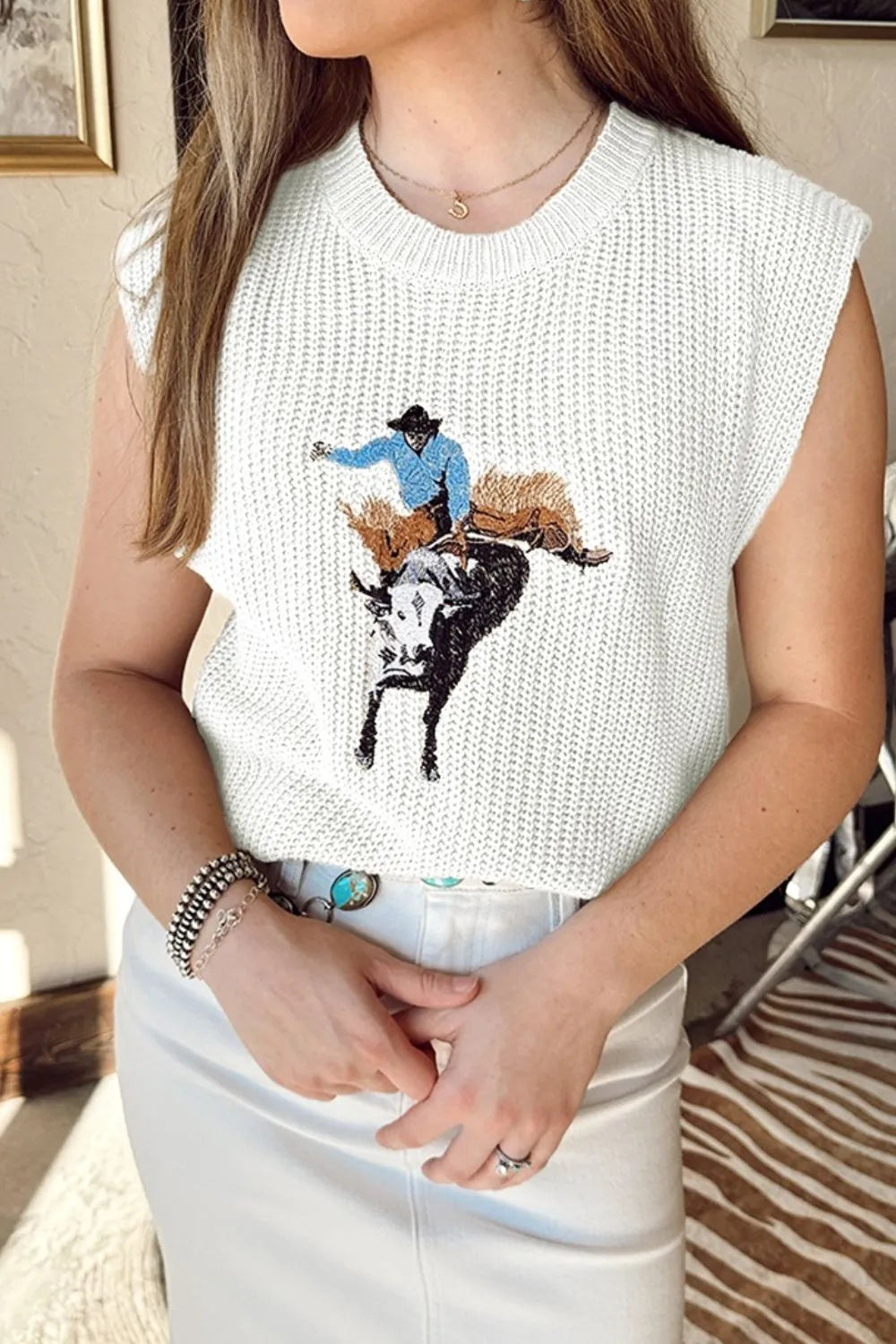 Person wearing a sleeveless white top with a graphic of a cowboy on a cow.