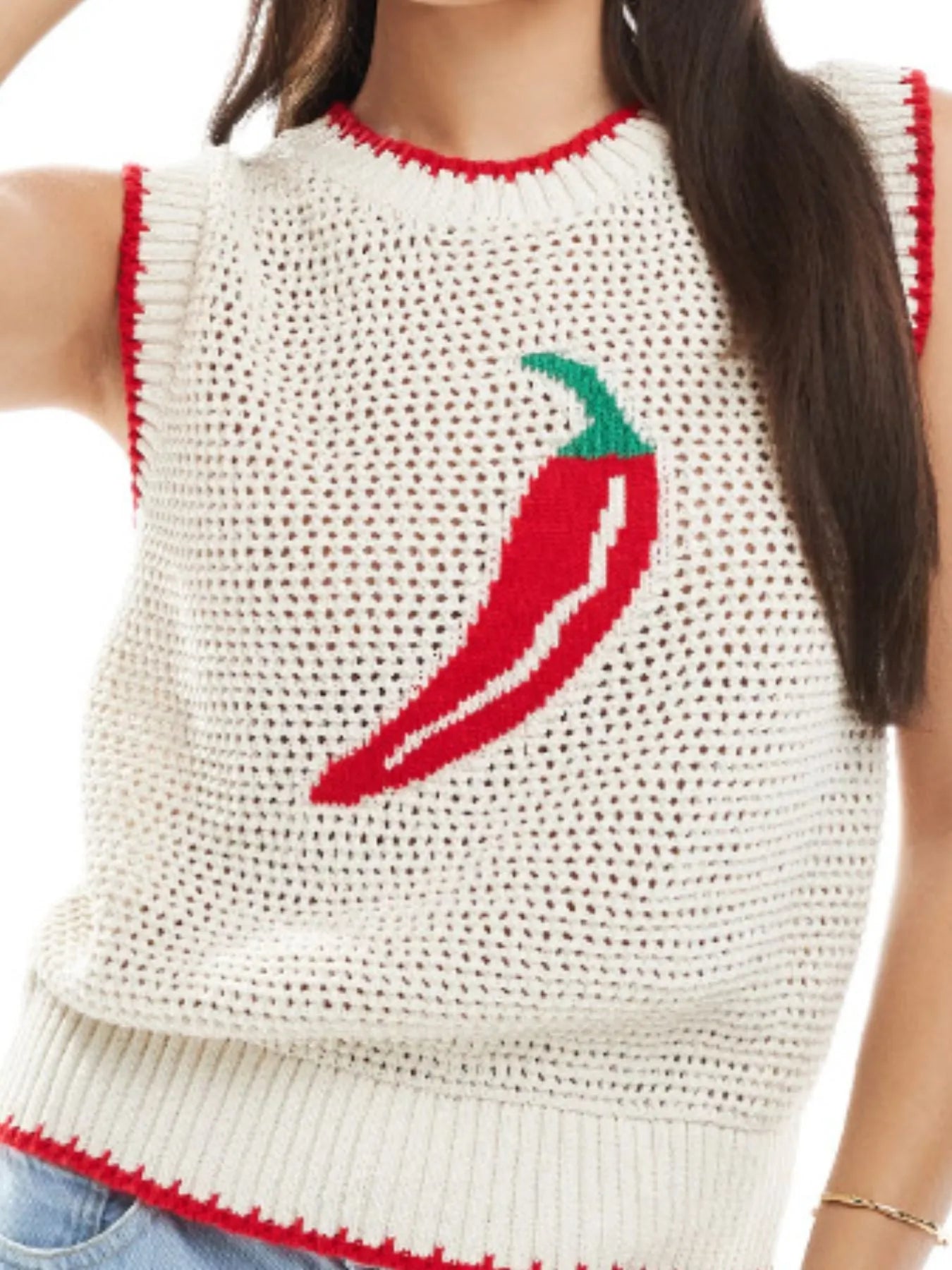 Person wearing a white sleeveless sweater with a red chili pepper design.