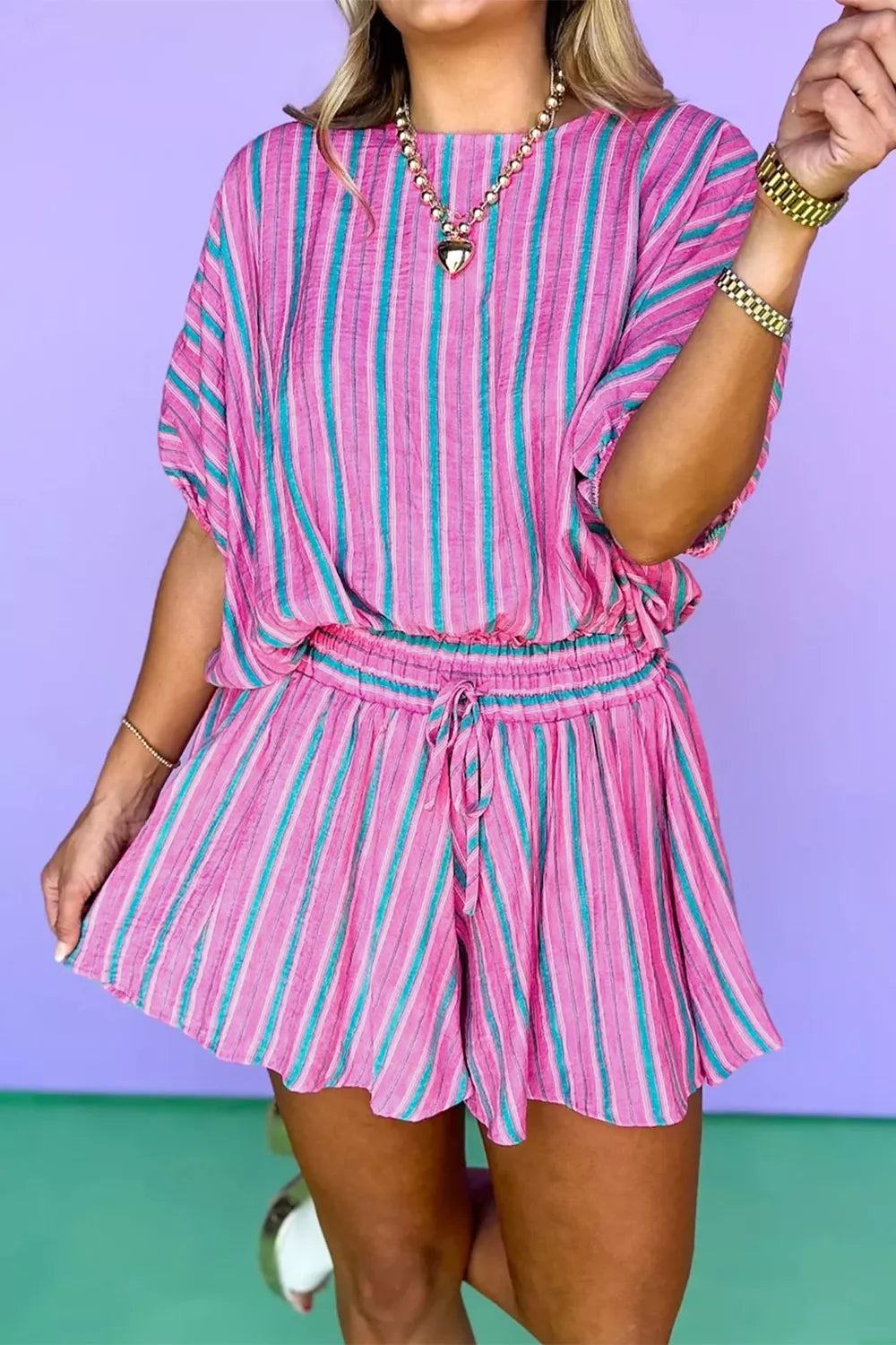 Person wearing a pink and blue striped romper against a purple and green background