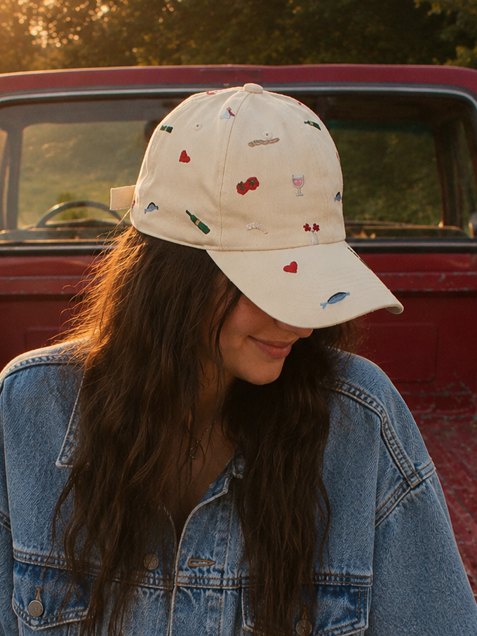 Person wearing a denim jacket and cap sitting in the back of a red truck.
