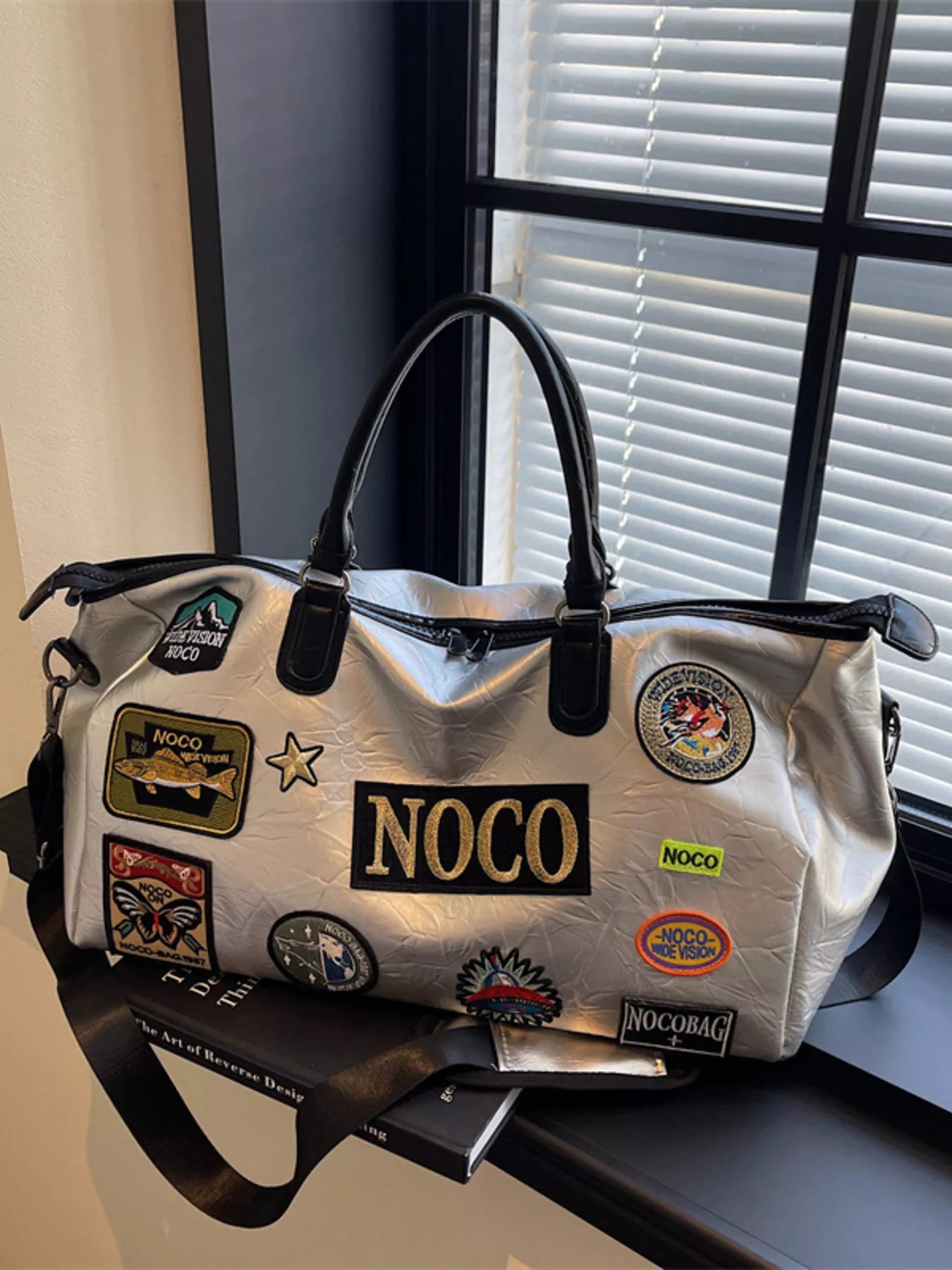 White bag with various patches, including a prominent 'NOCO' patch, on a surface.
