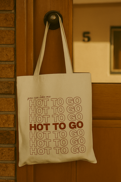 Retro-style canvas tote bag hanging on a motel door handle, featuring the phrase “you can take me hot to go” the Chappel Roan song in stacked red text.