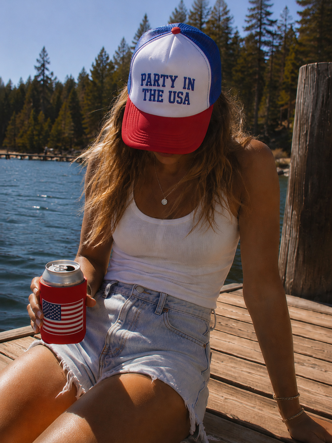 Person wearing a 'Party in the USA' cap by a lake