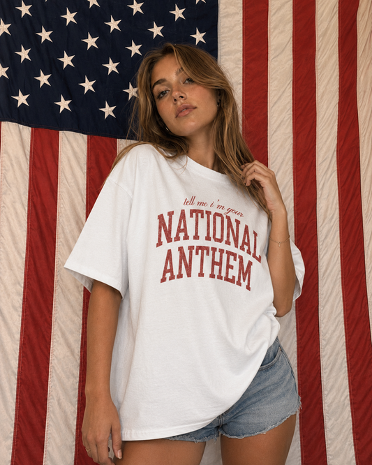 Person wearing a white t-shirt with 'National Anthem' text in front of an American flag